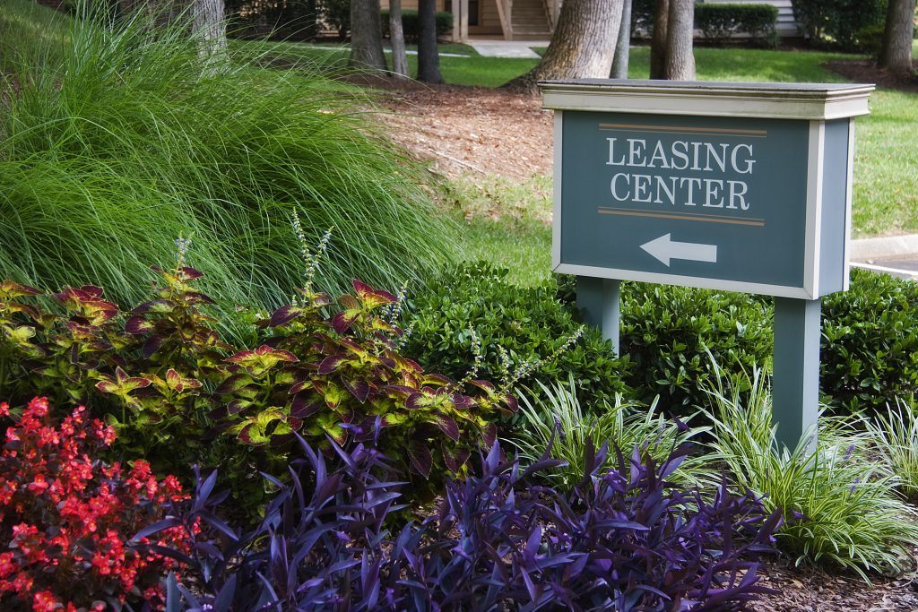 A sign that says leasing center in front of some bushes