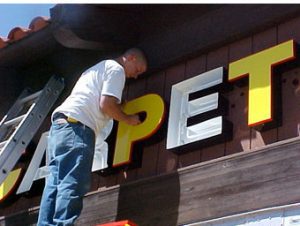 A man is painting the letters on the side of a building.