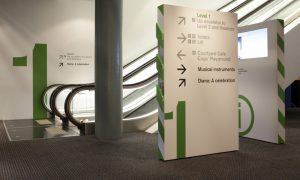 An escalator and a green wayfinding sign in a lobby.