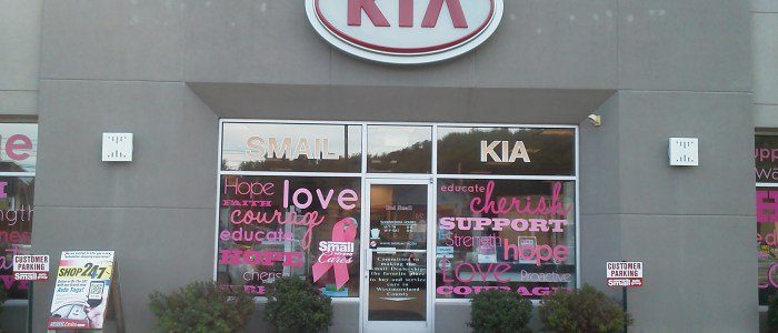 A kia dealership with pink ribbons on the windows.