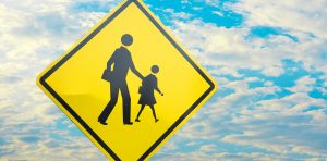 A yellow sign with an image of a person and child crossing.