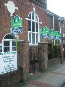 A row of brick buildings with green and white signs on them.