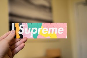 A person holding up a supreme sticker.